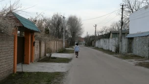 一人の女性が家や木々の間を道路を歩く 村の通り — ストック動画