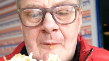 Gözlük ve parlak giysiler aç yaşlı adam hevesle kapalı pasta veya pizza yiyor.