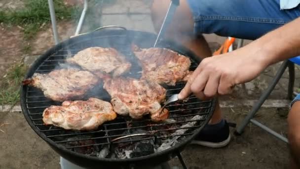 グリル料理 肉ステーキ男は 金属格子の上の小さな屋外グリルで バーベキューで石炭の上にロースト大きなおいしい肉ステーキをひっくり返します 週末のリラクゼーションコンセプト — ストック動画