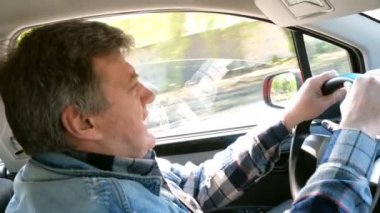 Yetişkin adam arabasını sürüyor, direksiyonu çeviriyor ve sürprizbir şekilde geleceğe bakıyor. Yolcu koltuğundan görünüm.