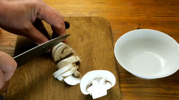 人間の手は キッチンナイフで木製のキッチンボード上の部分にシャンピニヨンキノコをカットし 白いセラミックボウルに入れて — ストック動画