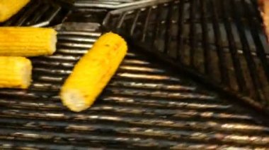 Koçan üzerindeki mısır ve domuz pirzolası dönen ızgara veya barbeküde kavrulur. Close. Hareket bulanıklığı.