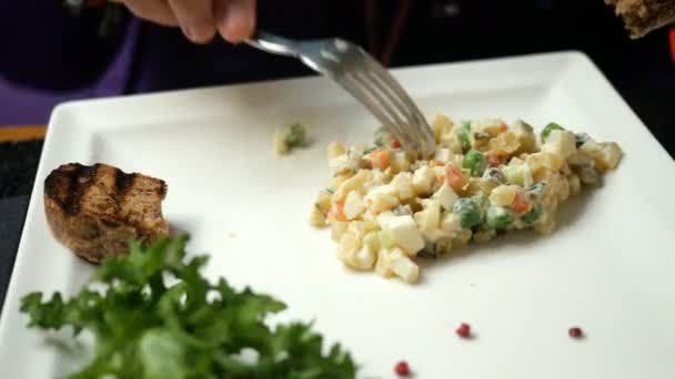 Смачна вечеря. Людина їсть традиційний салат для слов'ян Олів'є або салат з овочами та м'ясом в кафе або ресторані з білої тарілки . — стокове відео
