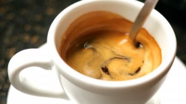 Kabarık köpüklü siyah sıcak espresso kahve beyaz bir kahve fincanı metal çay kaşığı ile karıştırılır.