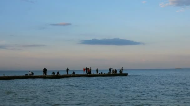 Вечер на Черном море. Люди ходят по волнорезу теплым спокойным летним вечером и любоваются закатом . — стоковое видео