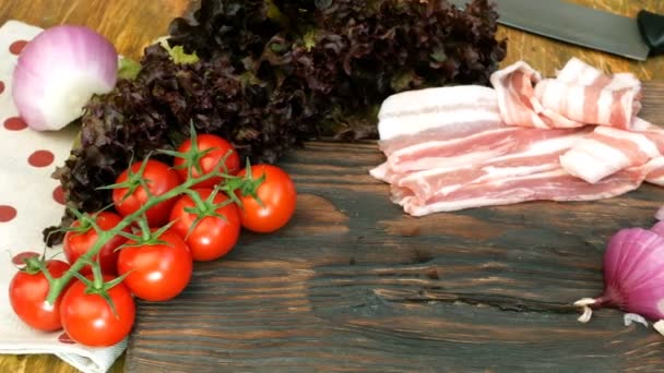 Zelfgemaakte gerechten. Producten voor heerlijk eten. Gesneden rauwe varkensvlees of rundvlees brisket, groenten: tomaten, sla, ui, knoflook, liggen op een houten keuken bord. In een rustieke stijl. — Stockvideo