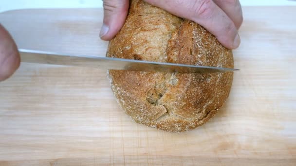 Domácí vaření. Mužské ruce řeže celý obilný chléb s kuchyňským nožem na dřevěné desce. Domácí pekárna nebo koncepce vaření organických přírodních potravin. Selektivní zaměření. — Stock video