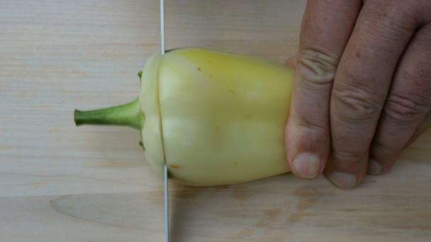 Zelfgemaakte gerechten. Menselijke handen knippen een zoete Bell gele peper, met een scherp keukenmes, op een houten oppervlak voor het koken. — Stockvideo