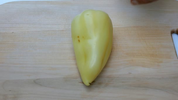 Zelfgemaakte gerechten. Menselijke handen knippen een zoete Bell gele peper, met een scherp keukenmes, op een houten oppervlak voor het koken. — Stockvideo