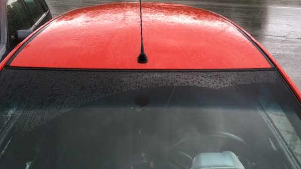 Gotas e jatos de chuva pingando no pára-brisas e no telhado de um carro de passageiros vermelho estacionado. Tempo chuvoso de outono. Close-up . — Vídeo de Stock