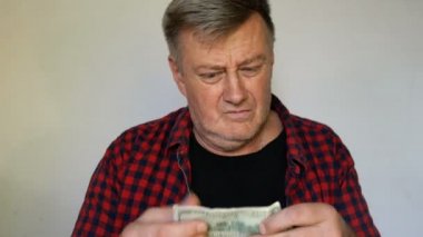Gri saçlı eksantrik kıdemli adam elinde yüz Amerikan doları bir banknot tutar ve bu konuda delicese mutlu. Yakın çekim portre. Açık arka planda.