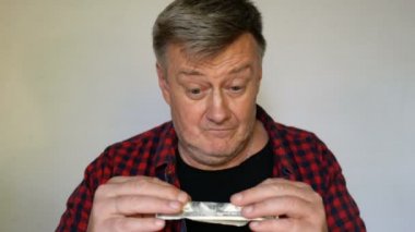 Gri saçlı eksantrik kıdemli adam elinde yüz Amerikan doları bir banknot tutar ve bu konuda delicese mutlu. Yakın çekim portre. Açık arka planda.
