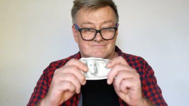 Gri saçlı eksantrik kıdemli adam elinde yüz Amerikan doları bir banknot tutar ve bu konuda delicese mutlu. Yakın çekim portre. Açık arka planda.