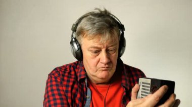 Expressive yetişkin kıdemli adam, eski radyo dinlerken ve farklı radyo istasyonları arıyor, kulaklık ile, şarkı ve müzik beat hamle. Açık gri arka planda. Close.