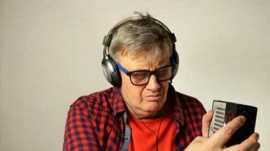 Expressive yetişkin kıdemli adam, eski radyo dinlerken ve farklı radyo istasyonları arıyor, kulaklık ile, şarkı ve müzik beat hamle. Açık gri arka planda. Close.