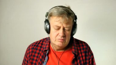 Etkileyici yetişkin kıdemli adam, onun kulaklık müzik dinler, birlikte şarkı ve müzik ritmine hareket eder. Açık gri arka planda. Close. Açık havada.