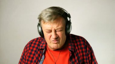 Etkileyici yetişkin kıdemli adam, onun kulaklık müzik dinler, birlikte şarkı ve müzik ritmine hareket eder. Açık gri arka planda. Close. Açık havada.