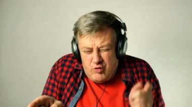 Etkileyici yetişkin kıdemli adam, onun kulaklık müzik dinler, birlikte şarkı ve müzik ritmine hareket eder. Açık gri arka planda. Close. Açık havada.