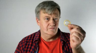 Kıdemli adam elinde prezervatif tutarak ve işaret, ve şehvet ile gülümsüyor, kameraya bakarak. Yaşlı yaşta aktif cinsel yaşam kavramı.