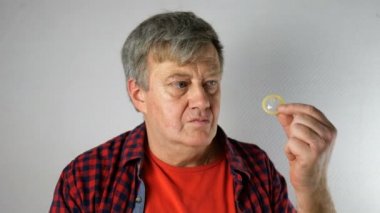 Kıdemli adam elinde prezervatif tutarak ve işaret, ve şehvet ile gülümsüyor, kameraya bakarak. Yaşlı yaşta aktif cinsel yaşam kavramı.