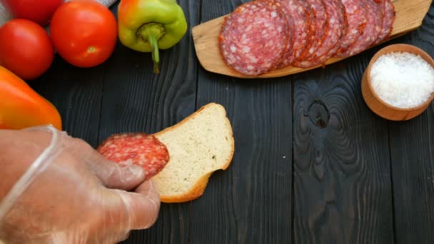 Zelfgemaakte keuken. Menselijke handen bereiden sandwich van gehakte salami en tomaat. Concept van het maken van fastfood. — Stockvideo