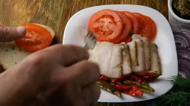 Hemlagat kök. Göra smörgås. Mänskliga händer gör smörgås med fläskis, tomater och pesto, som ligger på vit maträtt på brunt träbord. — Stockvideo