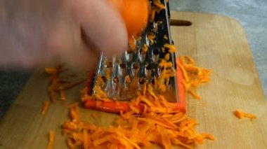 İnsan elleri, çorba veya salata yapmak için tahta kesme tahtasındaki metal rende çiğ havuç rendeliyor. Havuç ovuyorum. Vejetaryen sağlıklı yiyecekler pişirmek. Yakın plan..
