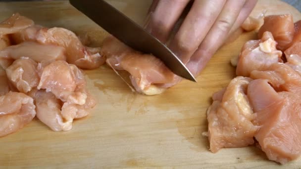 Les mains humaines coupant sur cube, poitrine de poulet tendre crue ou filet avec couteau de cuisine tranchant en bandes sur planche à découper en bois. Gros plan. — Video