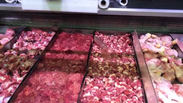 Diferentes partes de carne de pollo cruda, corazón de pollo, pierna, filete y despojos detrás de un escaparate de vidrio en el refrigerador en el mercado de carne o supermercado. Primer plano . — Vídeos de Stock
