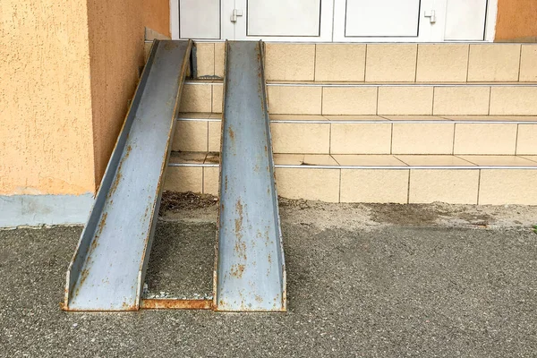 Old rusty metal ramp for entry of wheelchairs and baby carriage, over steps in residential building. People protection. Close-up. Outdoors.