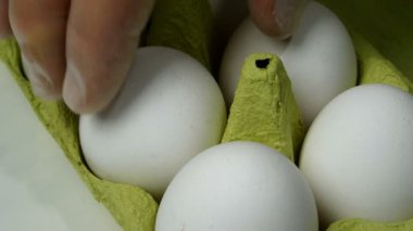 Şefler kauçuk koruyucu eldivenlerle kahvaltı için karton yumurta tepsisinden iki beyaz tavuk yumurtası alırlar. Ev yapımı yemek. Yakın plan..