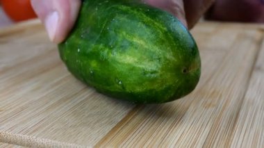 Aşçı elleri, salatalığı mutfak bıçağıyla kesti. Tahta kesme tahtasında kahvaltıda sebze vejetaryen salatası pişirmek için. Yakın plan..