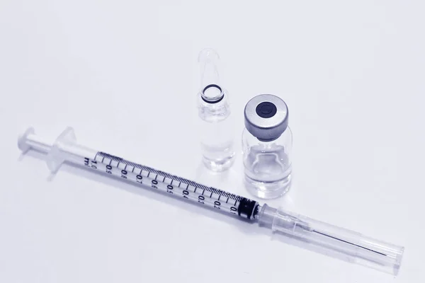 Ampulle mit Medikamenten oder Impfstoff und 1 ml Plastikspritze mit Nadel auf weißem Hintergrund, Farbe blau Stockbild