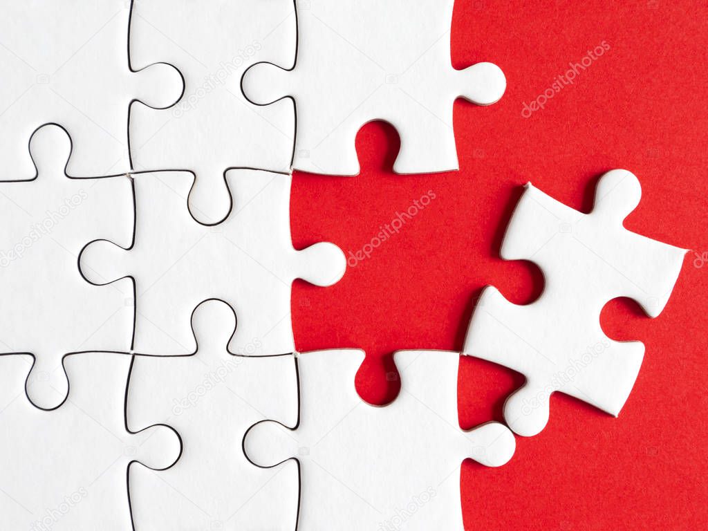 Closeup one white jigsaw puzzle beside missing jigsaw group on red background (Business Concept)