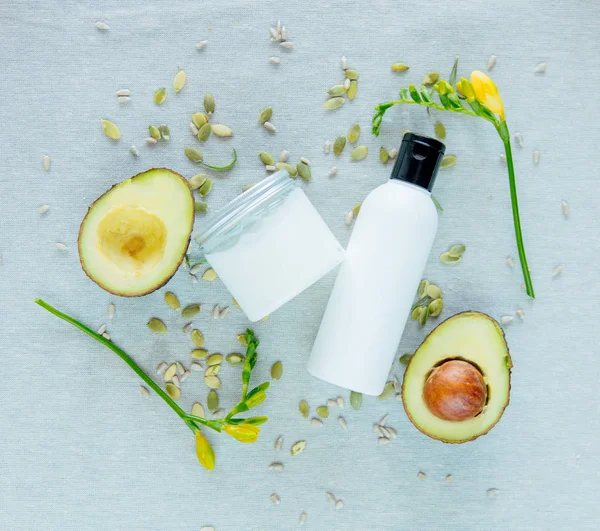 Cream bottles with organic avocado, seeds and flowers on grey table