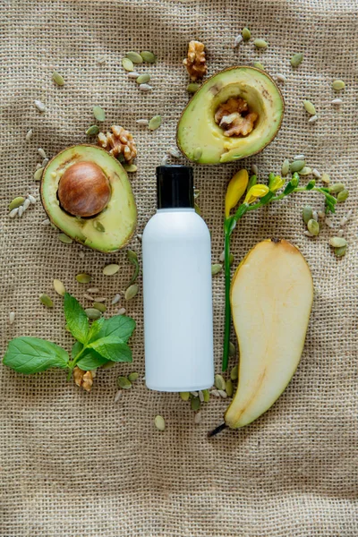 Cream bottle with organic avocado, seeds and walnuts on jute table