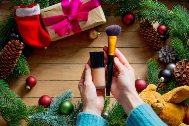 Erkek makyaj fırça ve Vakfı Şubesi ile Noel oyuncak, baubles, çam kozalakları ile arka planda tutan eller.