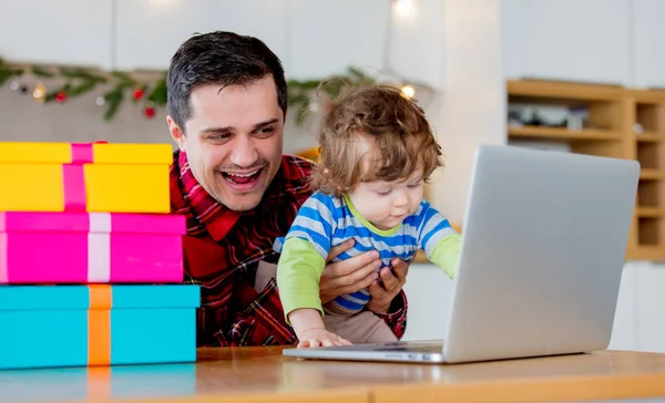 Father and son looking for Chritmas gifts in laptop computer sitting in kitchen at home.