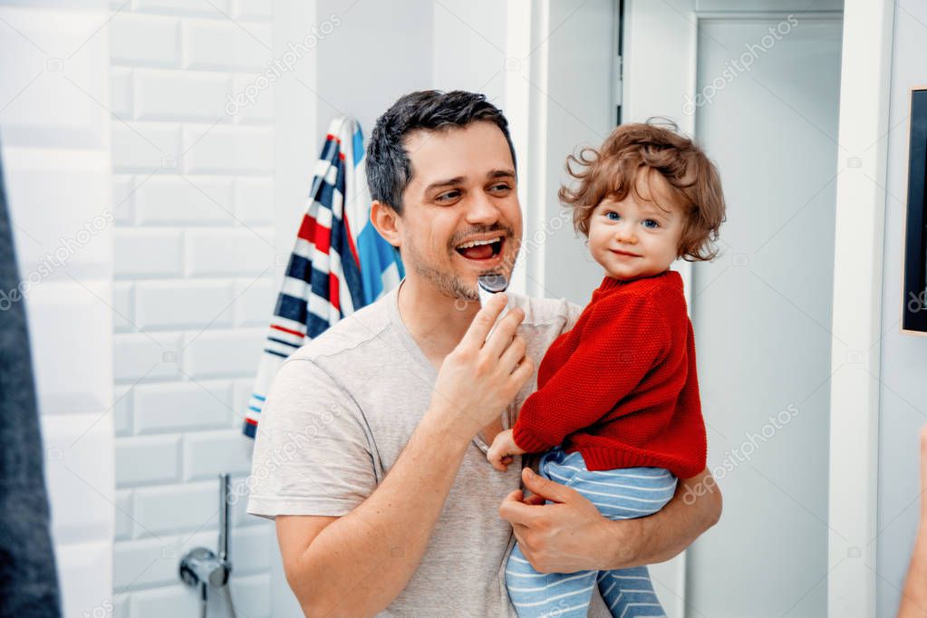 Middle age father holding toddler sun and shaving in the morning in bathroom 