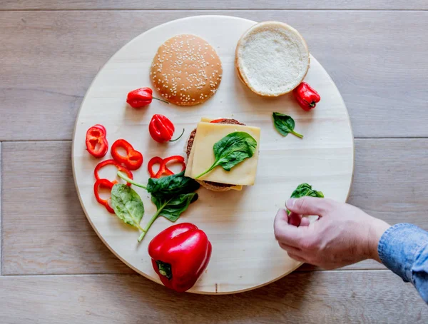 View as male hand holding hamburger ingredients and pepper on wooden background. Above view