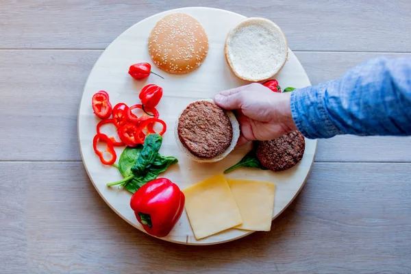 View as male hand holding hamburger ingredients and pepper on wooden background. Above view