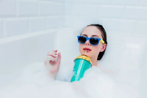 Femme avec cocktail et lunettes de soleil couchées dans une baignoire en mousse — Photo