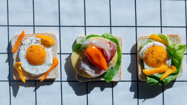 three sandwiches with tomatoes, omlette,ham and cheese on checkered background. Above view