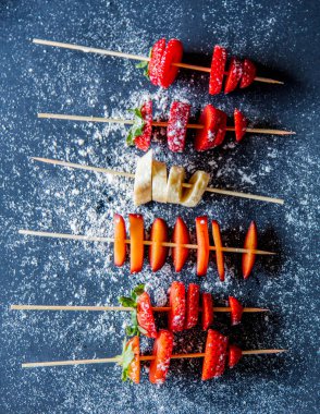 gri arka planda sopalarla çilek ve muz