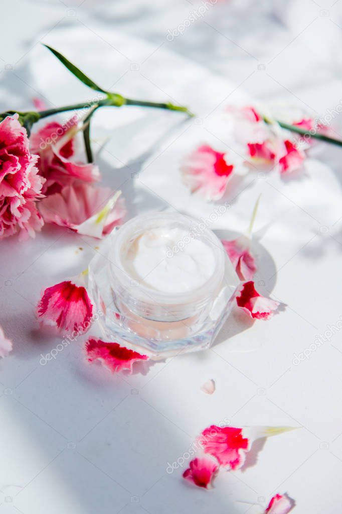Skin care cream in boolte and dianthus flowers around on white b