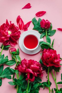 Pembe arka planda şakayık çiçekleri olan beyaz bir fincan çay.