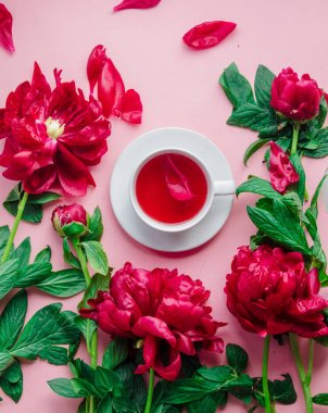 Pembe arka planda şakayık çiçekleri olan beyaz bir fincan çay.