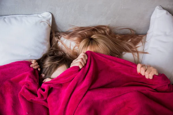 Mãe e filha se escondendo sob cobertor em uma cama — Fotografia de Stock