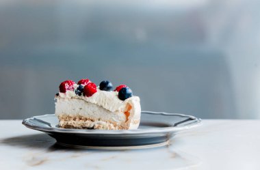 bir masada yaban mersini ve ahududu ile krem pasta parçası