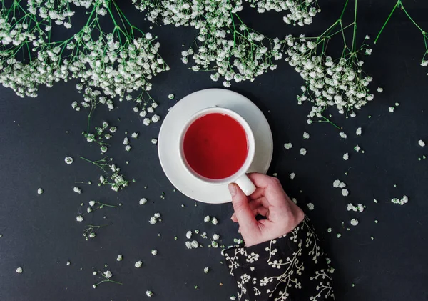 Femme tenant une tasse blanche de thé rouge près de Gypsophila paniculata f — Photo